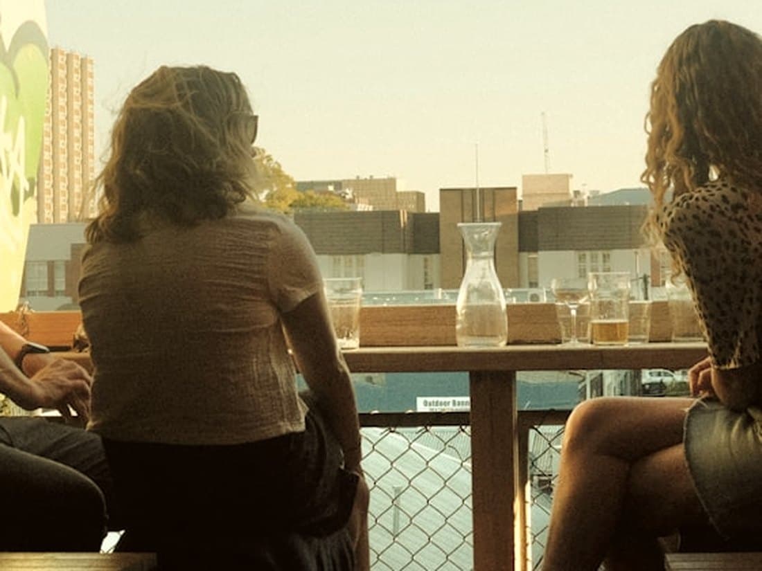 Friends sitting together at a rooftop rail at golden hour